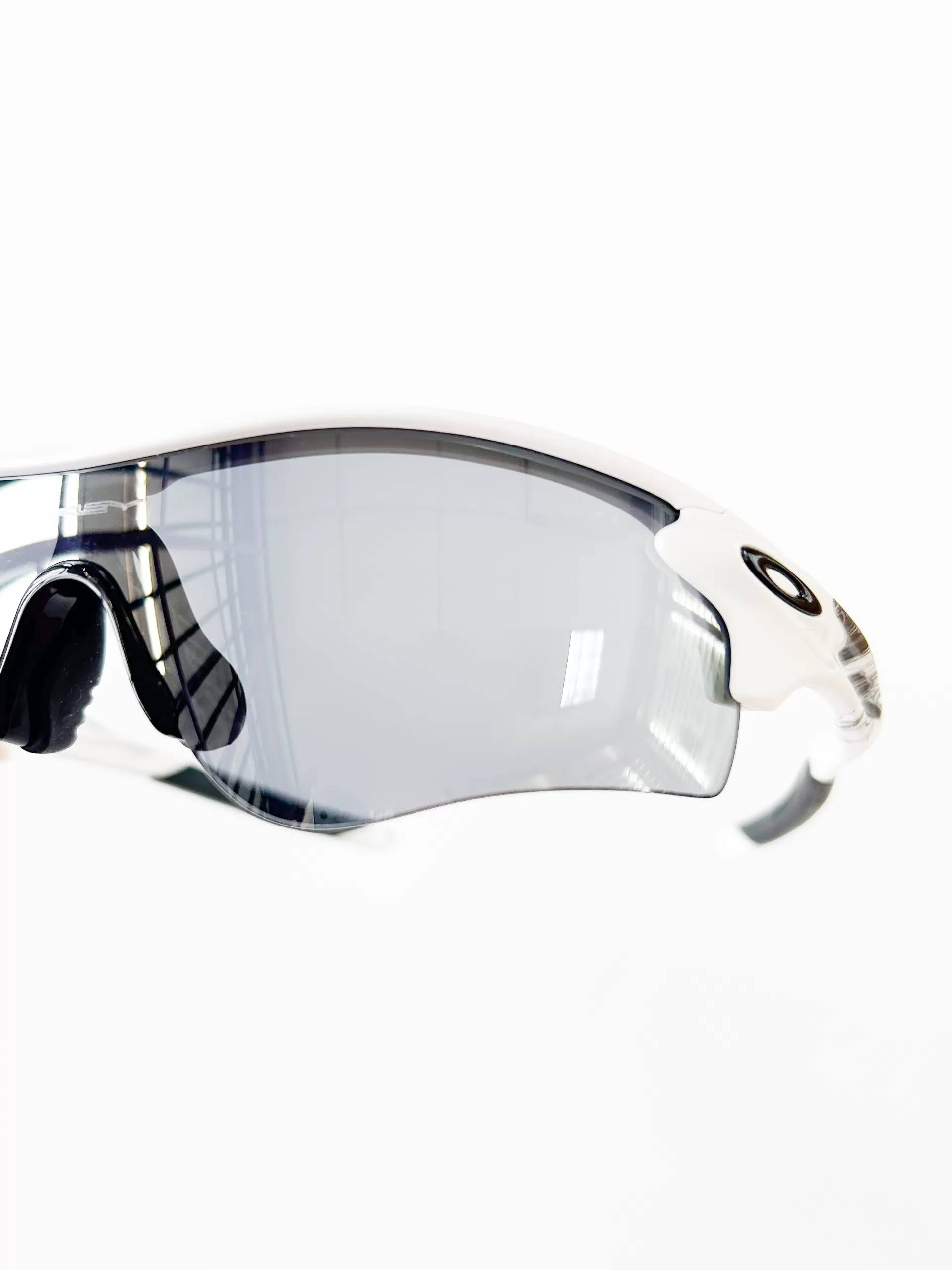 This image features a close-up view of a sleek, modern sports eyewear design. The sunglasses have a streamlined, wrap-around style with a semi-rimless frame that is predominantly white with black accents near the temples. The lenses are large and curved, providing extensive coverage and protection, and they have a gradient tint that transitions from darker at the top to lighter at the bottom. This design is ideal for active lifestyles, offering both functionality and a contemporary aesthetic suitable for sports and outdoor activities. The background is pure white, emphasizing the clean lines and the dynamic look of the eyewear.