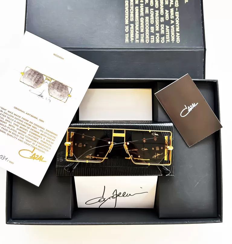 A pair of Cazal sunglasses displayed in a black presentation box, accompanied by a designer card, a sketch of the glasses, and a description booklet.