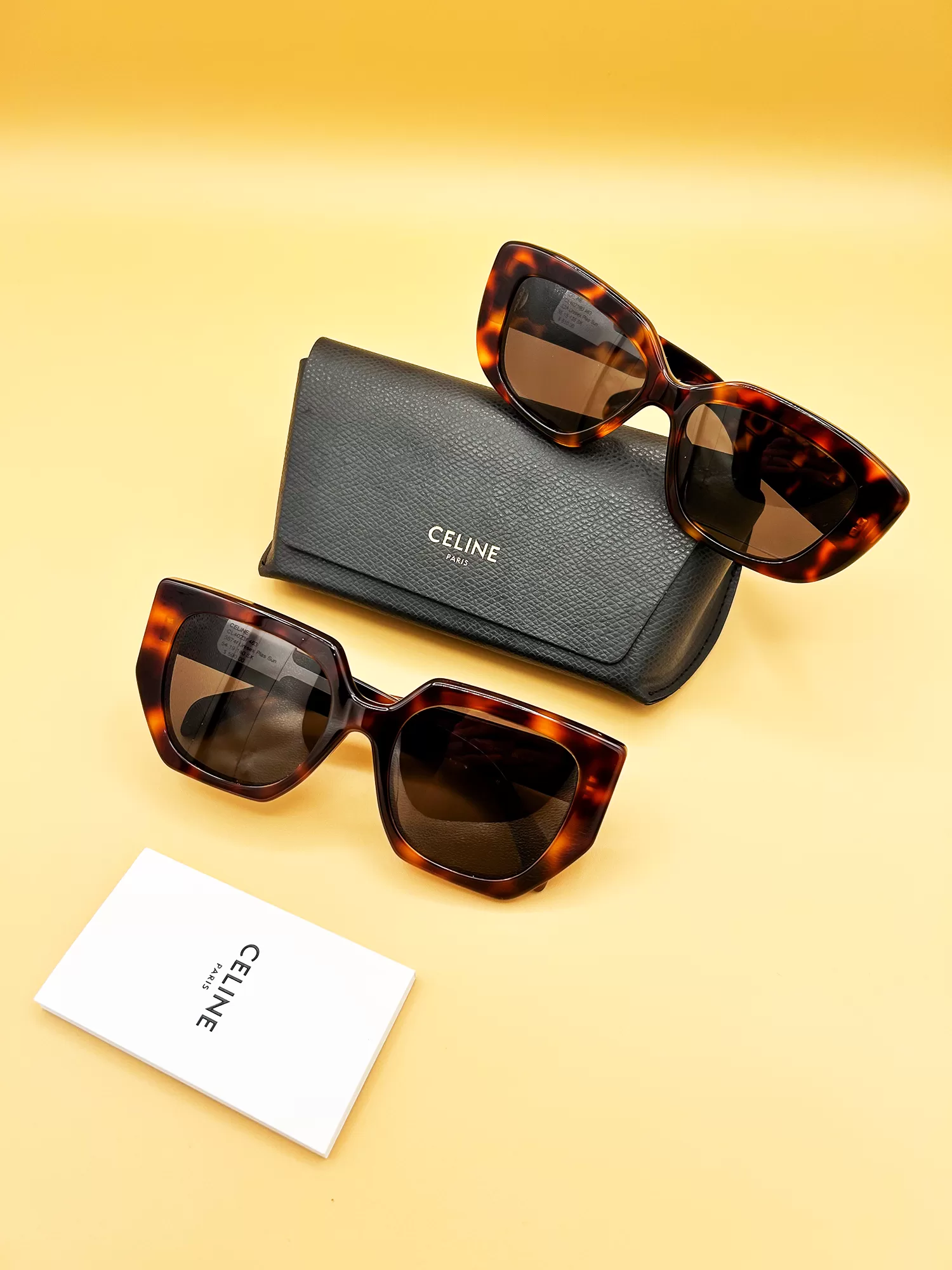 Two pairs of tortoiseshell Celine sunglasses displayed alongside a gray leather Celine pouch and a white brand card on a vibrant yellow background.