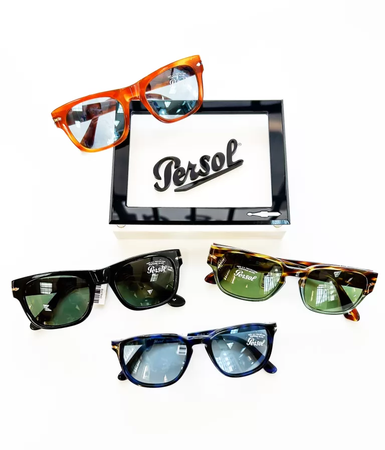 An assortment of Persol sunglasses and eyeglasses displayed on a white surface, featuring four different styles. Each pair has its own distinct frame color and design, including classic black, vibrant orange, tortoiseshell, and deep blue.