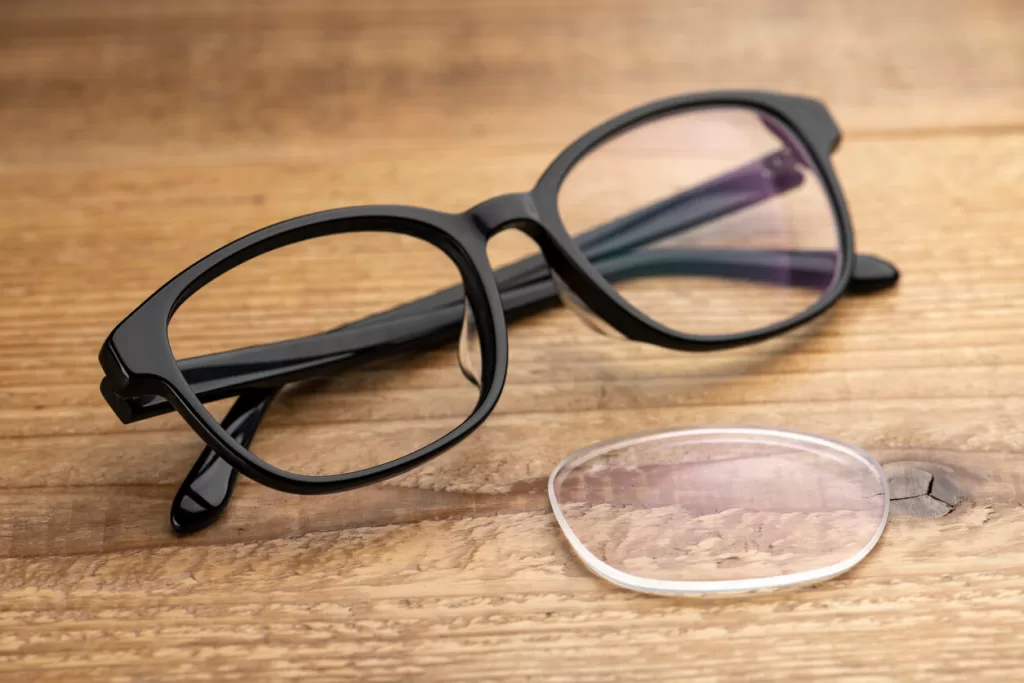 Eyeglass replacement lenses on a wooden table with black glasses