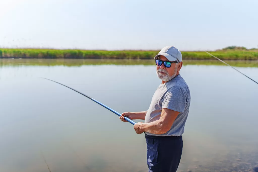 Man wearing Maui Jim sunglasses while fishing on the bank of a river