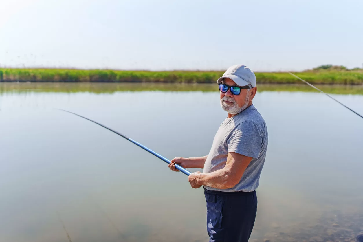 Man wearing Maui Jim sunglasses while fishing on the bank of a river