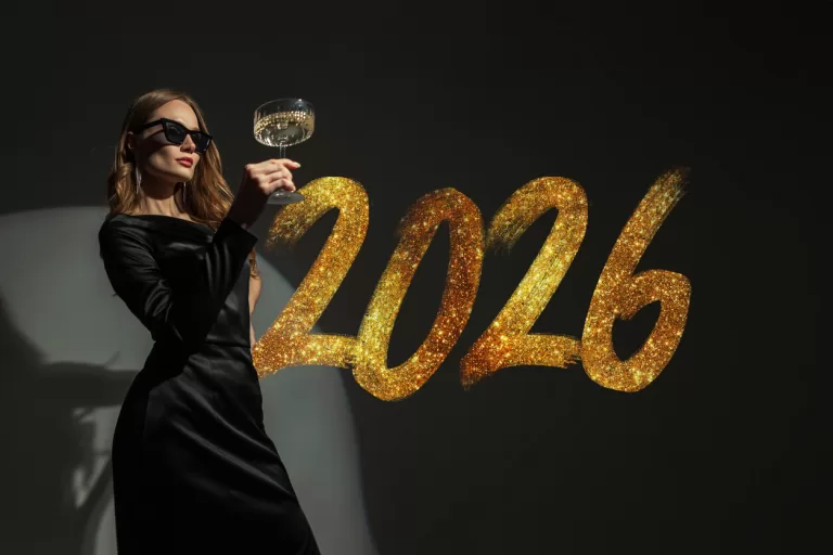 Elegant young woman in a black dress and luxury sunglasses holding a champagne glass to celebrate 2026
