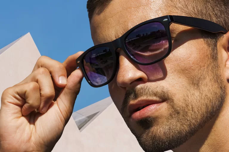 Unshaven man in sunglasses on the background of white architecture, sunglasses advertisement